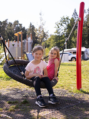 Two children sit on a basket swing at a playground